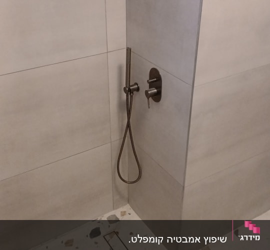 ראש מקלחת ידני על קיר אריחים בחדר רחצה
